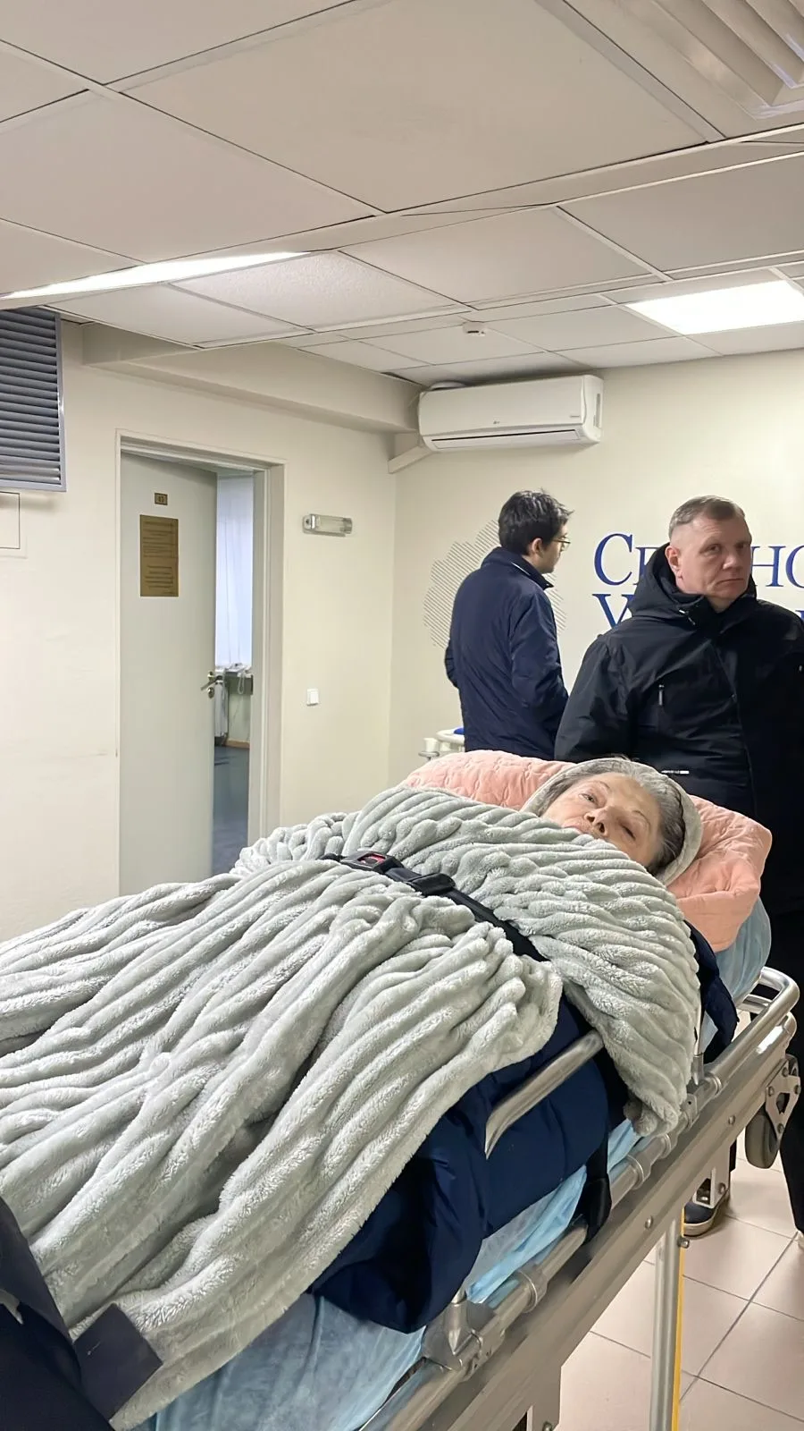 Женщина под пледом на медицинской каталке в коридоре